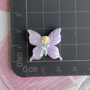Macro detail of a purple resin butterfly accessory with rose, shown on a scale ruler