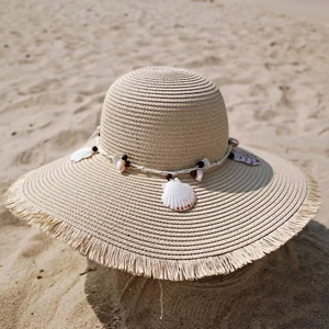 Women's wide brim straw sun hat with shell charms and frayed edges on beach background