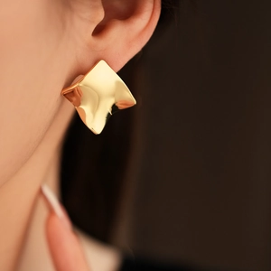 Gros plan d'un modèle portant une boucle d'oreille carrée torsadée géométrique plaquée or