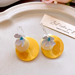 Close-up of yellow acrylic geometric earrings with white flower detail on ceramic plate
