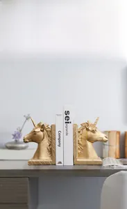 Detailansicht goldener Einhorn-Buchstützen auf einem Schreibtisch mit Holztextur