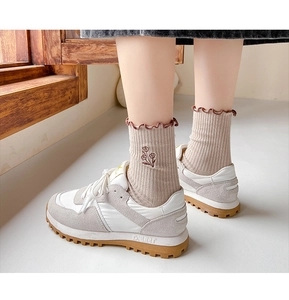 Detail of cream rib-knit socks with flower embroidery and ruffled cuffs with retro sneakers