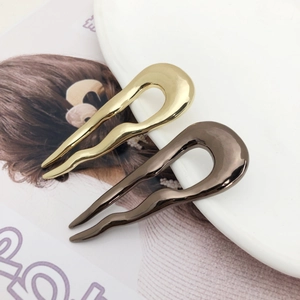 Minimalist U-shaped metal hairpins in gold and bronze finish on a minimalist background