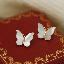 Macro shot of butterfly stud earrings with white mother-of-pearl and gold metal edges