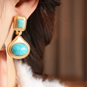 Detail shot of vintage golden earrings with turquoise texture stones on a female model