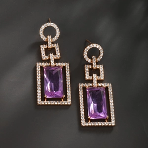 Détail de boucles d'oreilles géométriques dorées avec pierre zircon violette et cristaux