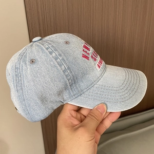 Detail of light blue washed denim baseball cap featuring pink embroidered text on front