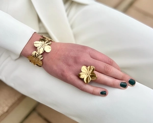 Detail view of gold flower bracelet and ring set worn with white suit blazer
