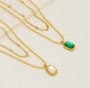 Close-up of double-layer gold necklaces featuring emerald green and white zircon pendants