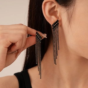 Détail de longues boucles d'oreilles à pompons noirs avec chaîne dorée et zircon sur modèle