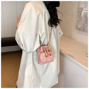 Detail of pink quilted bucket bag with chain strap and drawstring closure shown on model