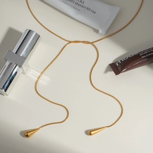 Détail du collier en Y chaîne serpent dorée avec pendentifs gouttes et cosmétiques