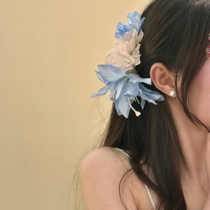 Pince à cheveux fleur en tissu bleu clair portée par un modèle pour un look de vacances