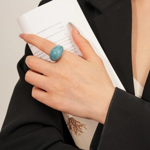 Gros plan d'une grande bague ovale en résine bleu sarcelle sur un doigt