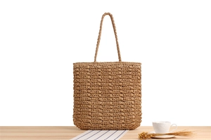 Detailed view of the woven texture and shoulder strap of this khaki straw tote bag