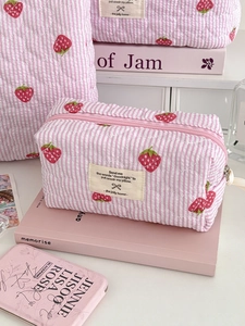 Pink striped quilted makeup bag with red strawberry print and zipper closure on a desk