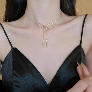 Close-up of golden bow necklace with fine snake chain and elegant long tassel pendants