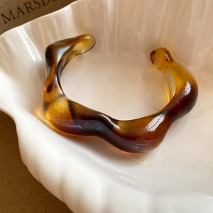 Macro detail of wave-shaped resin bangle featuring polished amber tortoiseshell texture