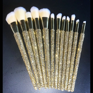Detail of 12 luxury makeup brushes with champagne gold rhinestone handles on black background