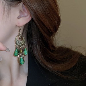 Close-up of bohemian bronze leaf earrings with green water-drop beads and tassels