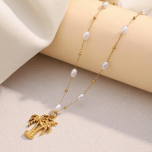 Detail of 18K gold-plated coconut tree pendant with pearls on a textured beige stand