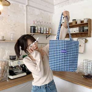 Blue and white checkered plaid wool tote bag with a purple label in a cozy cafe setting