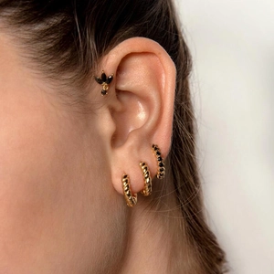 Macro detail of gold-plated twisted rope hoop earrings and black stone studs on ear