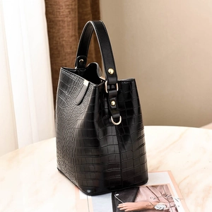 Chic black crocodile texture bucket handbag with gold hardware on marble surface