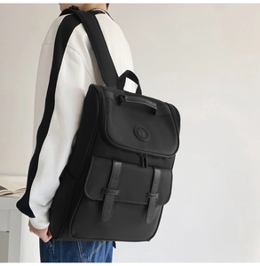 Side view of a black nylon backpack with leather buckles worn by a model in a minimal setting