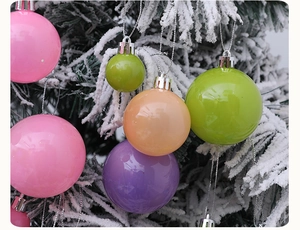 Boules de Noël aux couleurs macaron accrochées à une branche d'arbre enneigée