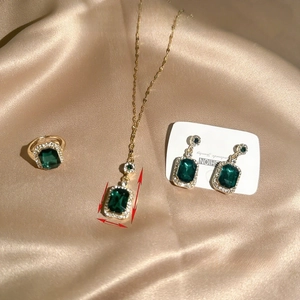 Detailed set of emerald necklace, earrings, and ring with halo stones on silk fabric