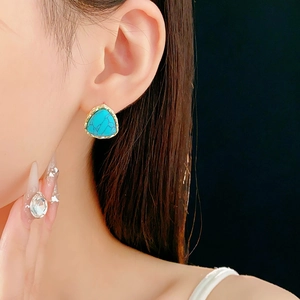Close-up of vintage gold triangle earrings with blue turquoise texture on a model