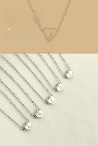 Detailed view of silver heart-shaped pendants with engraved letters on a soft cloth background