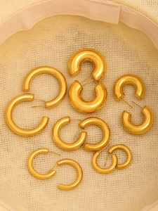 Detalle macro de aretes de aro en forma de C dorados de varios tamaños sobre fondo beige