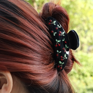 Detail of a black hair claw clip featuring sparkling rhinestone cherry motifs on hair