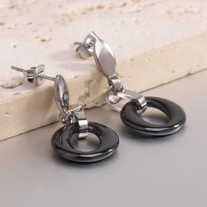 Elegant stainless steel earrings with black ceramic circular hollow pendants on stone surface