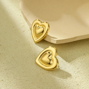 Close-up of golden heart earrings with high metallic luster on textured background