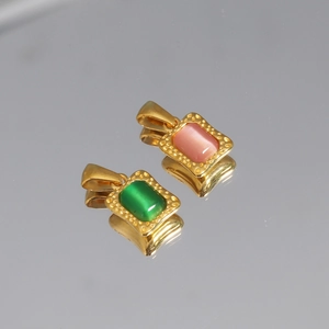 Detail of square gold pendants with pink and green cat-eye stones on reflective surface