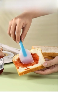 Detail of a silicone spatula spreading strawberry jam on toast in a cozy breakfast scene