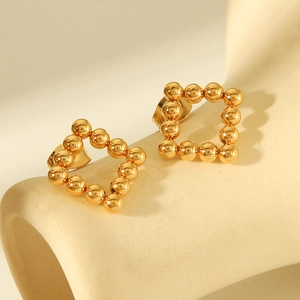 Detailed view of square-shaped golden beaded stud earrings on a beige ceramic stand
