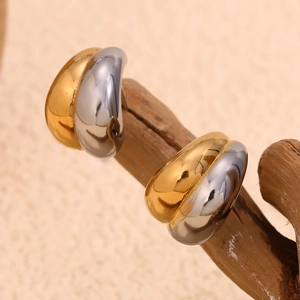 Polished gold and silver mixed metal teardrop earrings displayed on natural wood