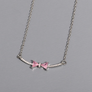 Macro shot of silver bow necklace pendant featuring pink zircon stone and link chain detail