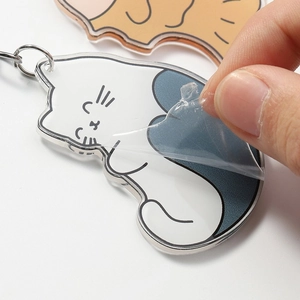 Detail showing removal of protective film from clear acrylic cat keychain with metal ring