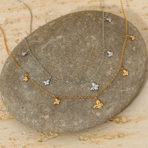 Elegante Schmetterlingsketten in Gold und Silber präsentiert auf einem glatten Kieselstein