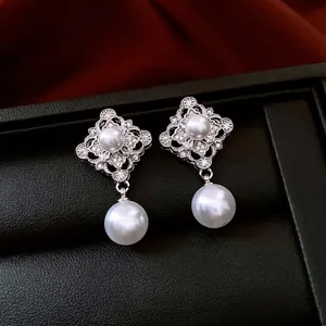 Lustrous drop pearl earrings with hollow diamond-set rhombus studs on leather