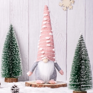 Pink knitted gnome figurine on wood slice with pine cones and winter snow scene decor