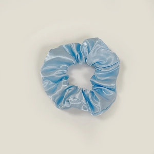 Macro view of light blue satin scrunchie showing glossy fabric texture and pleats