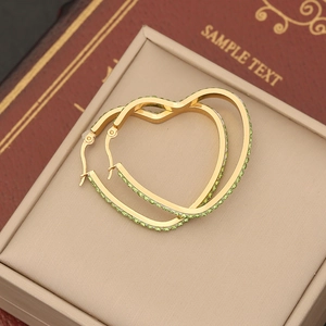 Golden heart hoop earrings with sparkling green rhinestones on a beige jewelry box