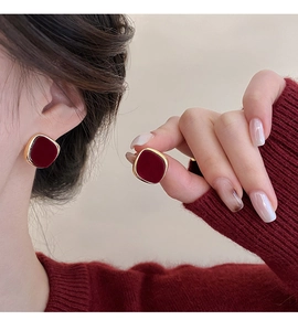 Close-up of elegant burgundy flocked square earrings with gold-plated metal edges on ear