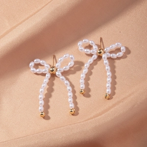Detailed close-up of French bow-shaped earrings with pearls on champagne silk fabric